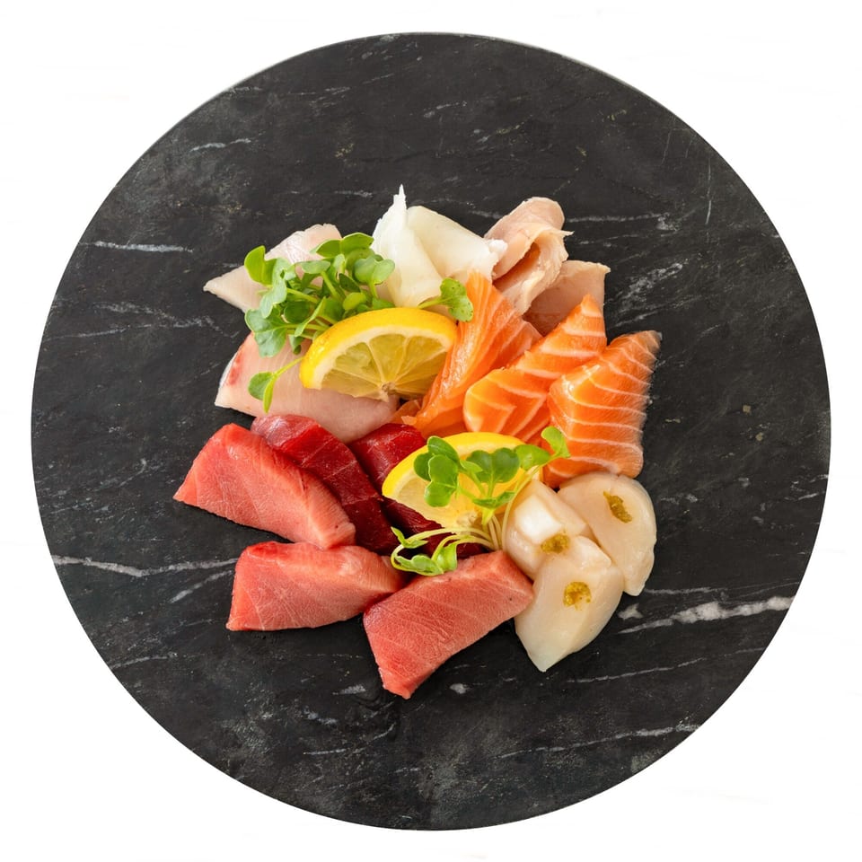Assorted sashimi platter with tuna, salmon, scallops, and white fish, garnished with lemon and greens.