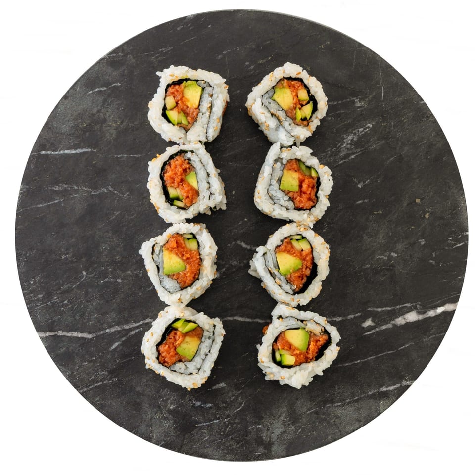Eight Pisces sushi rolls with spicy tuna and avocado, arranged on a dark marble plate.