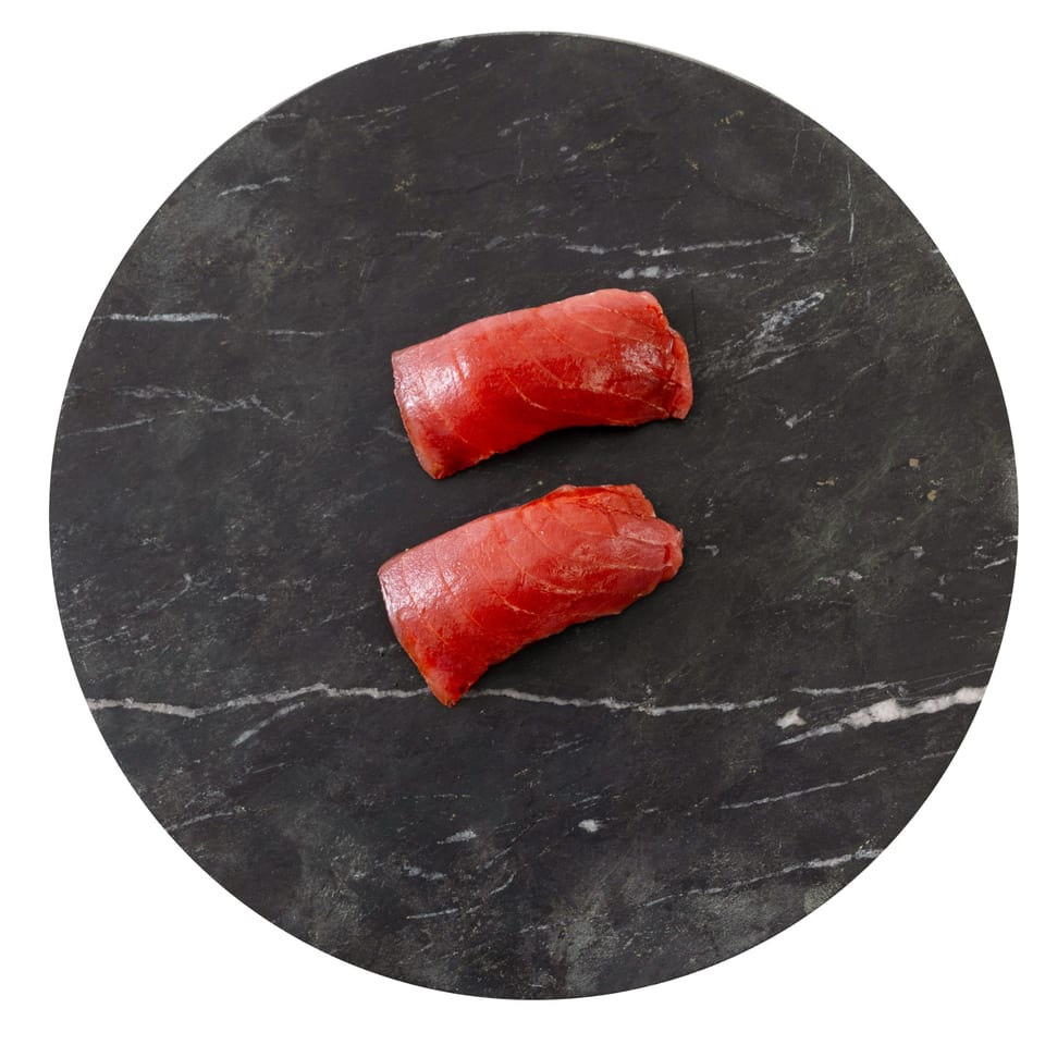 Two pieces of fresh, vibrant red tuna sashimi on a dark, circular marble slab.