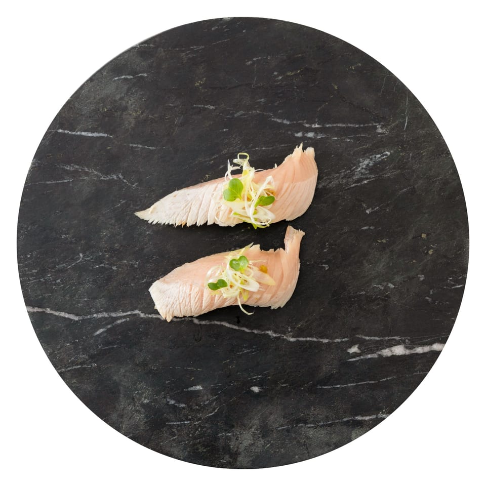 Two pieces of Pisces sushi, topped with green onions and sprouts, on a dark marble plate.