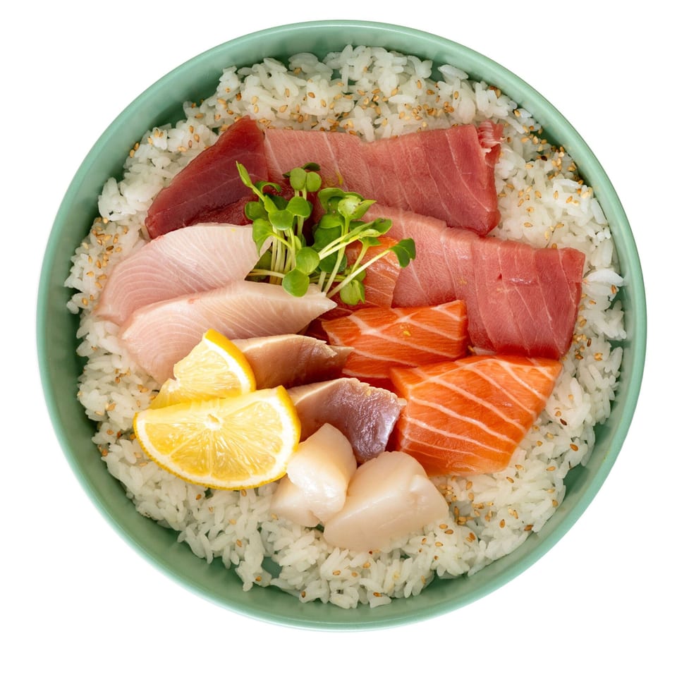 Overhead view of a Pisces chirashi bowl with various sashimi, rice, lemon, and microgreens.