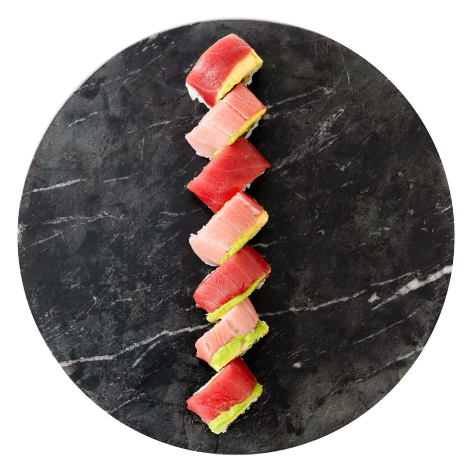 Tuna and avocado sushi rolls arranged diagonally on a round, dark marble plate.