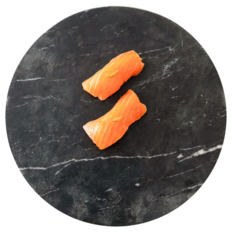 Two pieces of fresh salmon sushi with a dab of sauce on a dark, round marble plate.