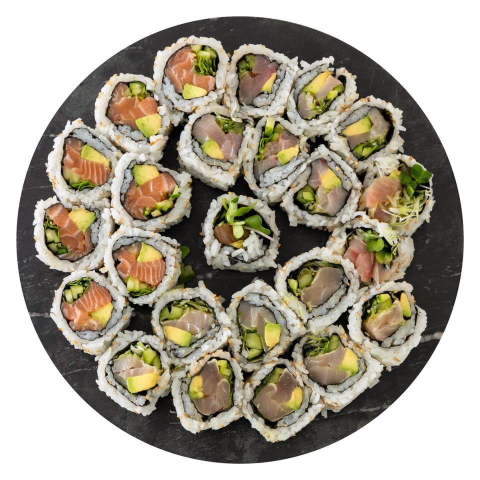 Assortment of Pisces sushi rolls with salmon, tuna, avocado, and greens on a dark round plate.