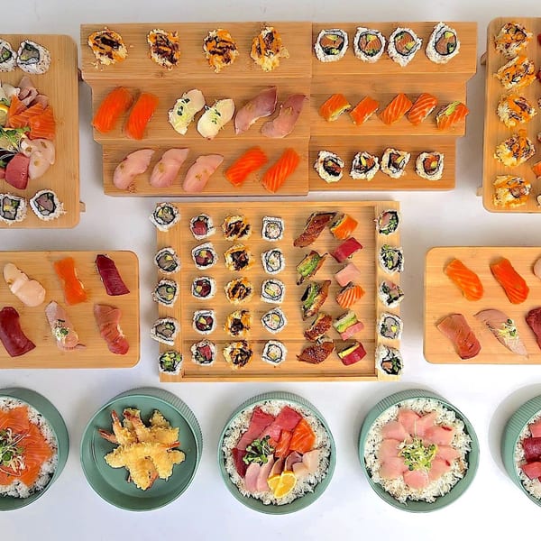 An overhead view of a large sushi and sashimi platter with various rolls, nigiri, and chirashi bowls.