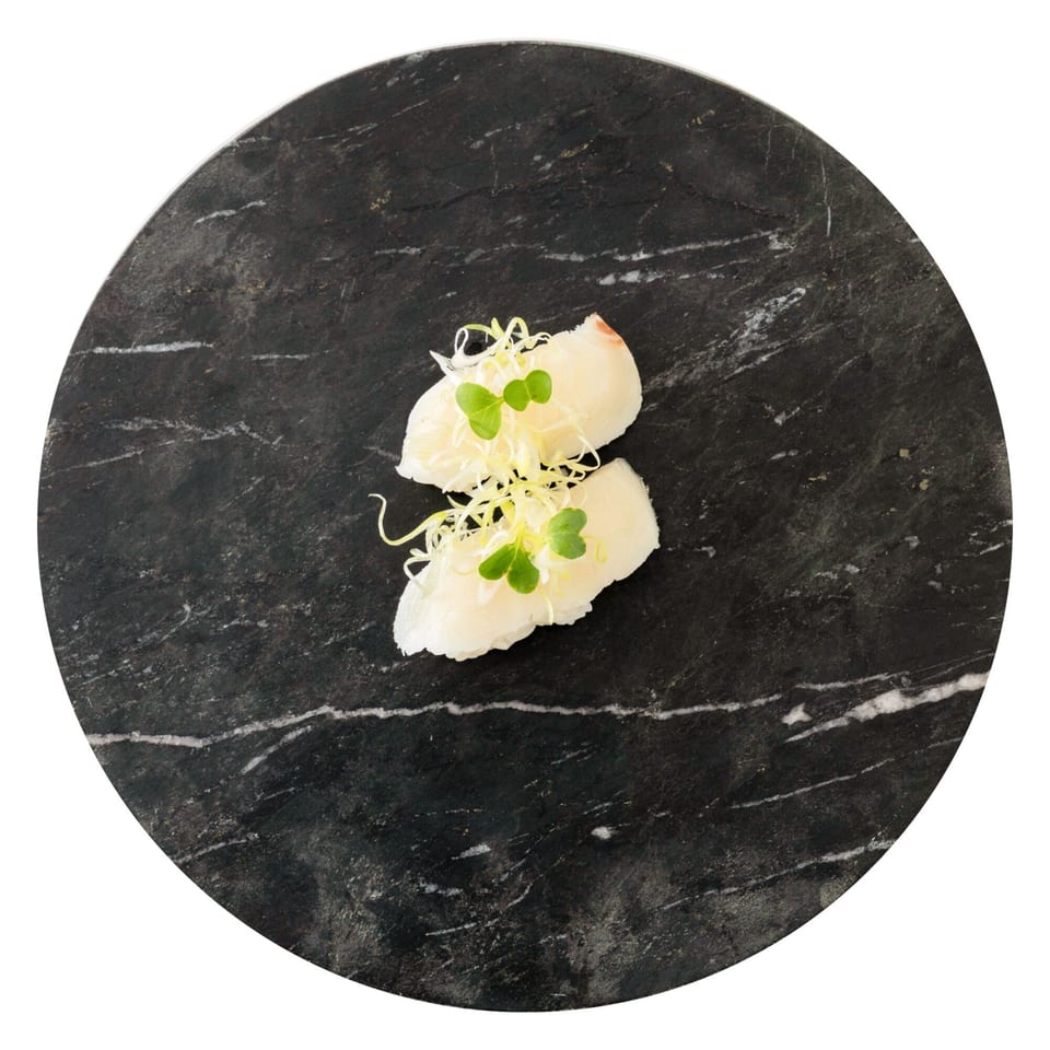 Two pieces of white fish sushi with green sprouts on a dark marble plate.