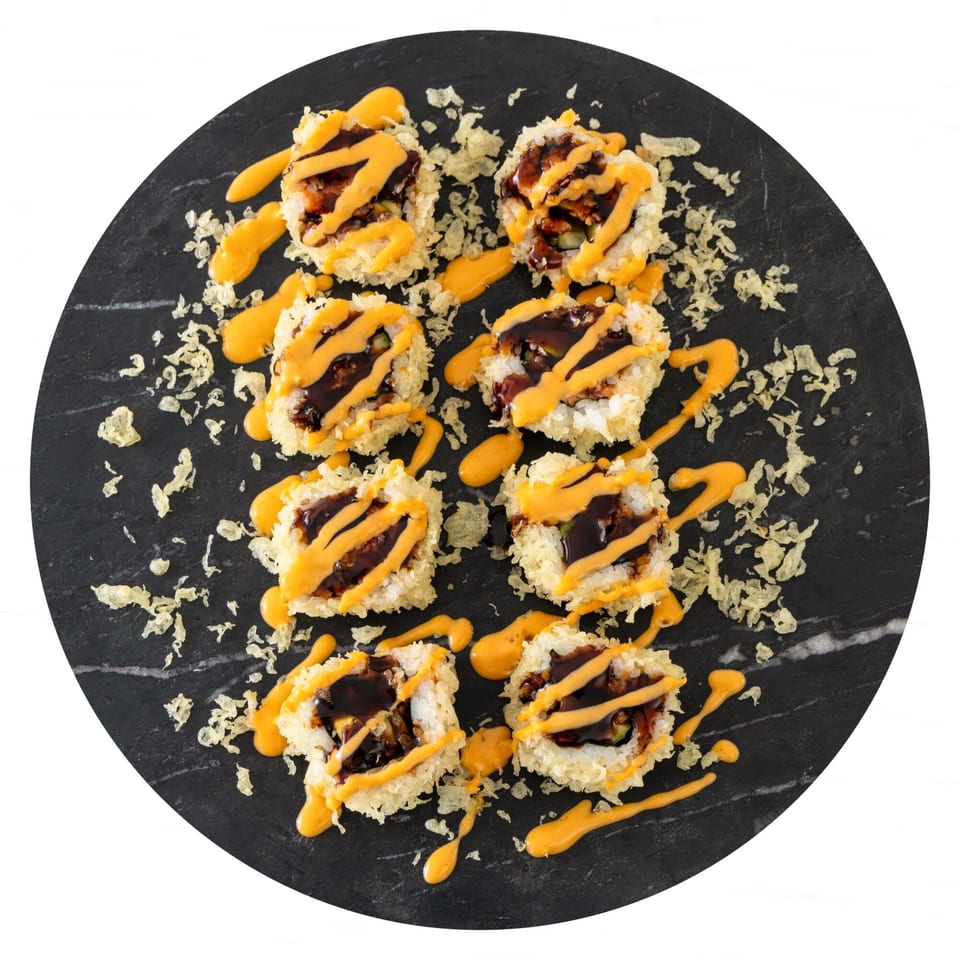 Eight pieces of Pisces sushi, drizzled with dark and orange sauces, on a black marble plate.
