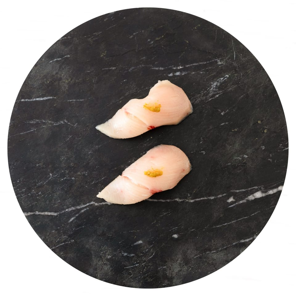 Two pieces of white fish sushi with yellow garnish on a dark, marbled serving plate.