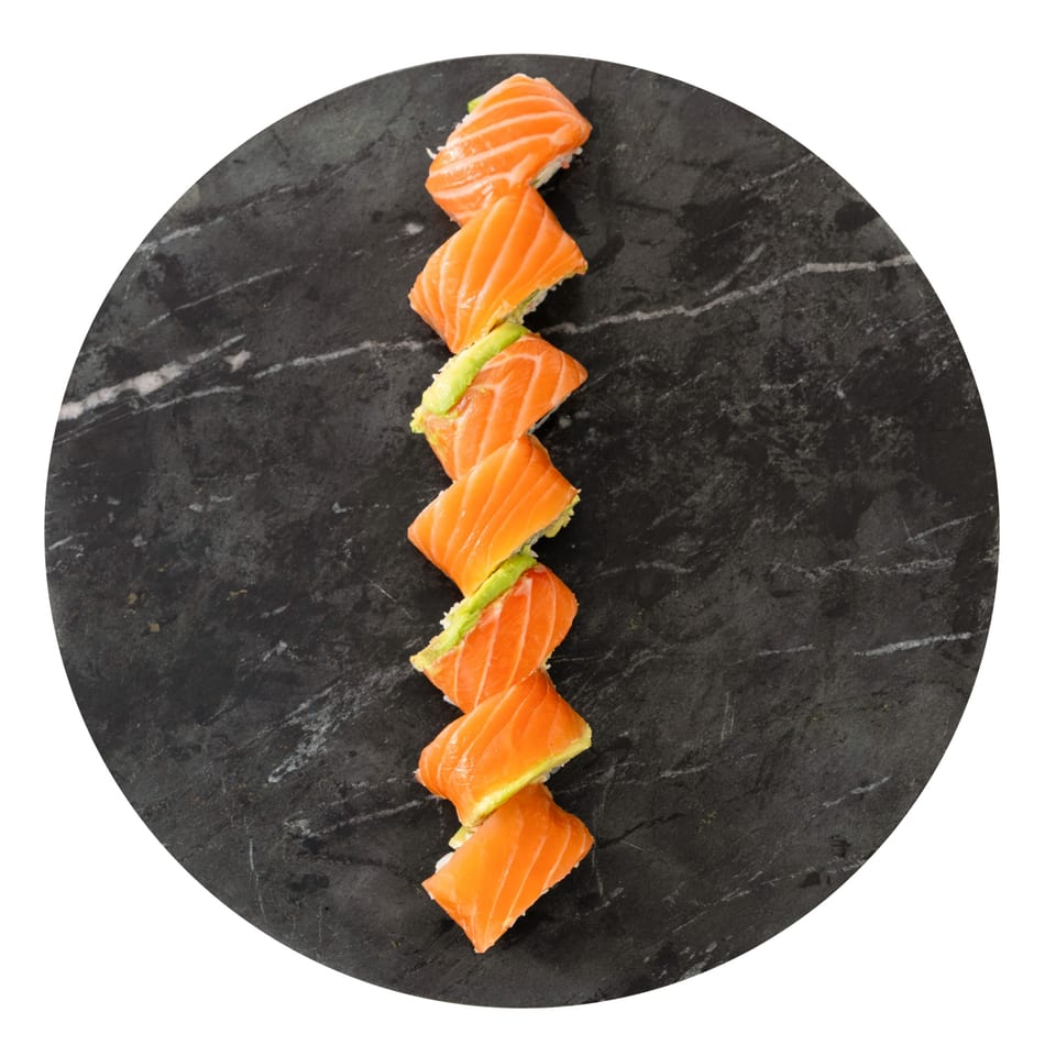 Salmon and avocado sushi rolls arranged in a line on a dark circular stone plate.