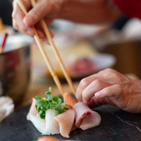 A chef's hands meticulously arrange fresh sushi and microgreens on a dark serving platter.