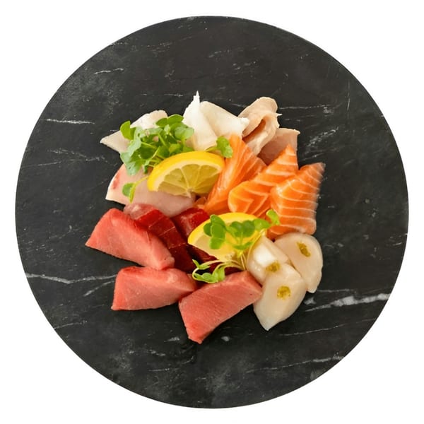 Assorted sashimi platter with tuna, salmon, and scallops, garnished with lemon and microgreens on a black slate.