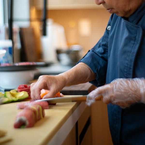 A Pisces sushi chef in a blue uniform prepares sushi rolls and fresh ingredients.
