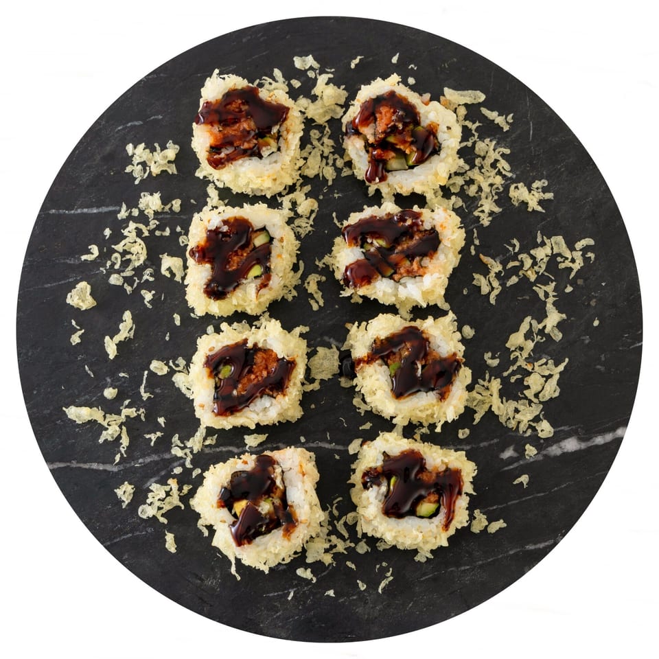 Eight pieces of Pisces sushi, drizzled with dark sauce, on a round black slate.