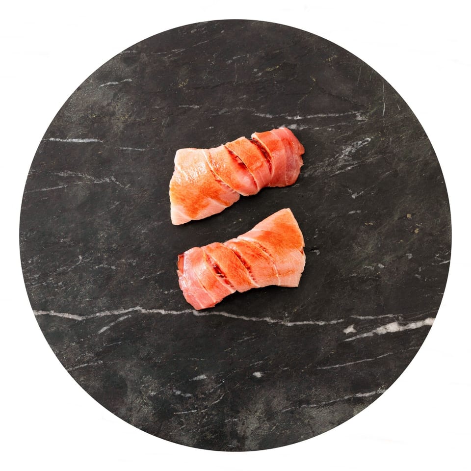 Two pieces of sliced raw tuna, with red and pink hues, on a dark marble surface.