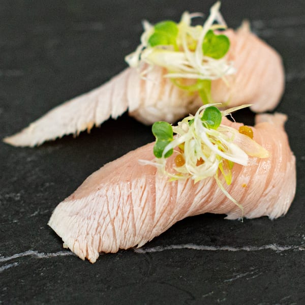 Two pieces of Pisces sushi, topped with green onions and microgreens, on a dark stone surface.