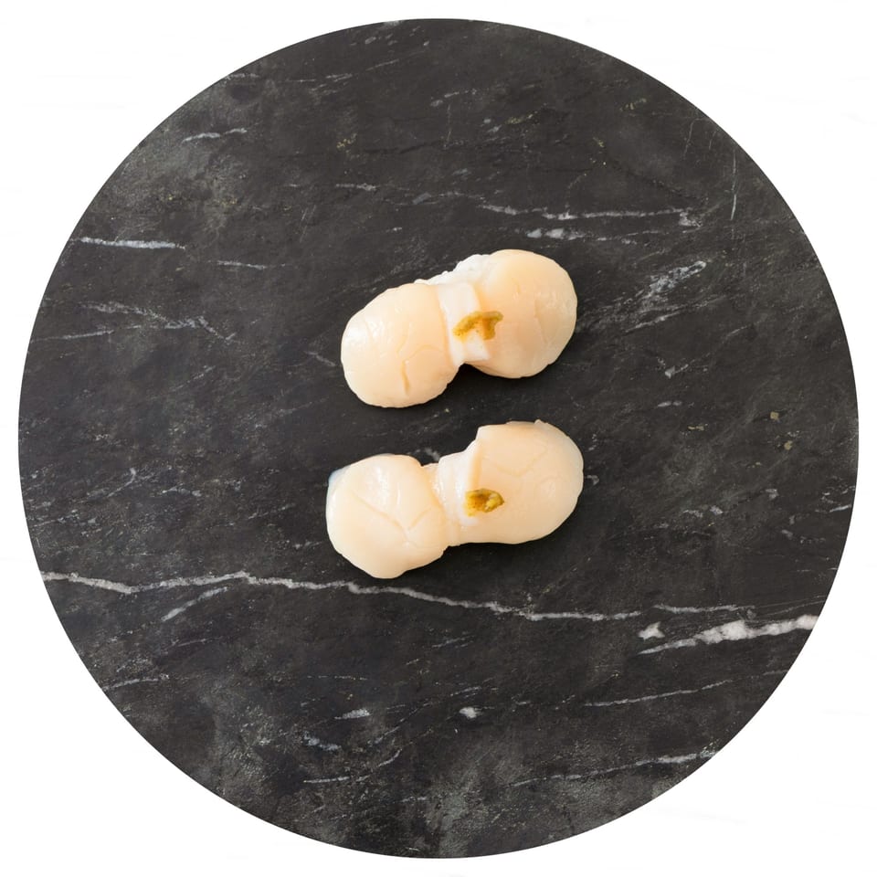 Two pieces of scallop nigiri sushi with a dab of green garnish on a dark marble plate.