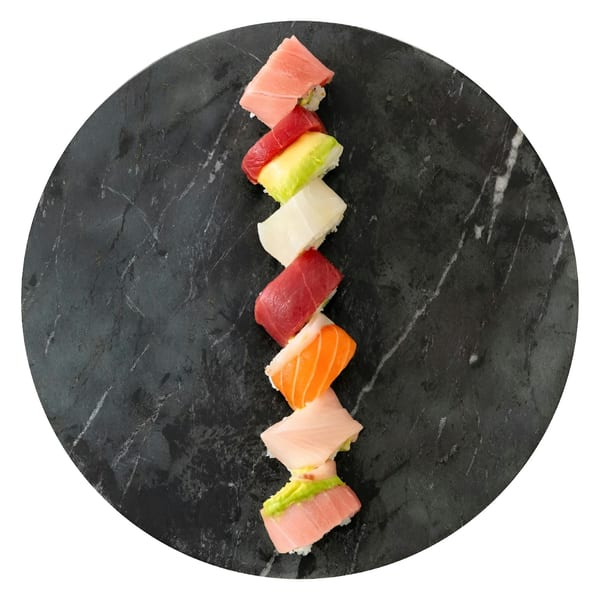 Assorted sushi pieces, including tuna, salmon, and avocado, arranged on a dark marble plate.