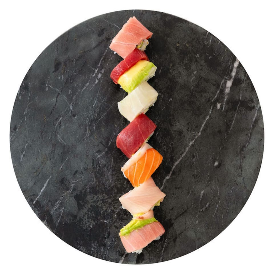 Assorted sushi rolls with tuna, salmon, and avocado on a dark circular stone plate.