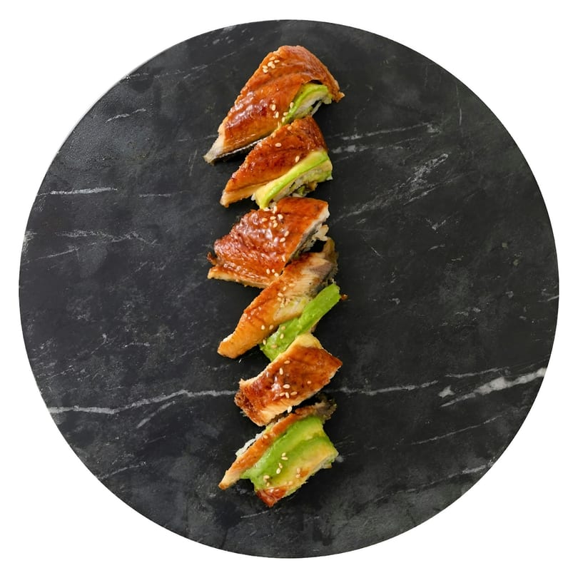 Six pieces of eel and avocado sushi with sesame seeds, arranged on a dark marble plate.
