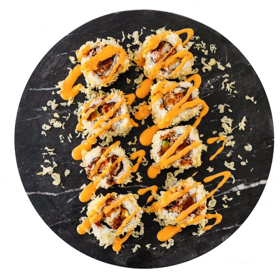 Eight pieces of Pisces sushi rolls, drizzled with orange sauce and tempura flakes on a black plate.